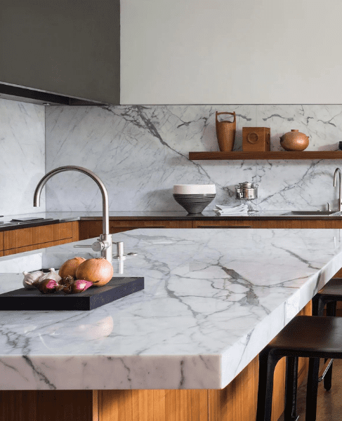 Modern kitchen with a marble worktop and splashback, wooden cabinetry, and minimalist styling.