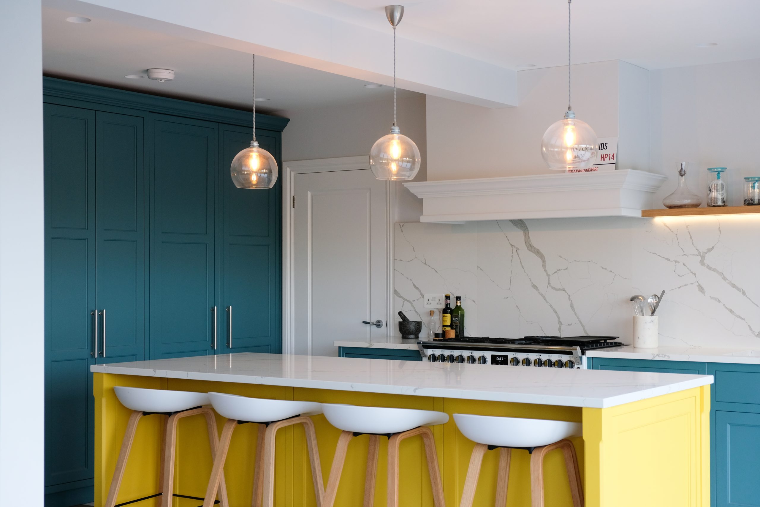 Modern yellow kitchen with bold yellow island, teal cabinets and white quartz worktop with marble veining
