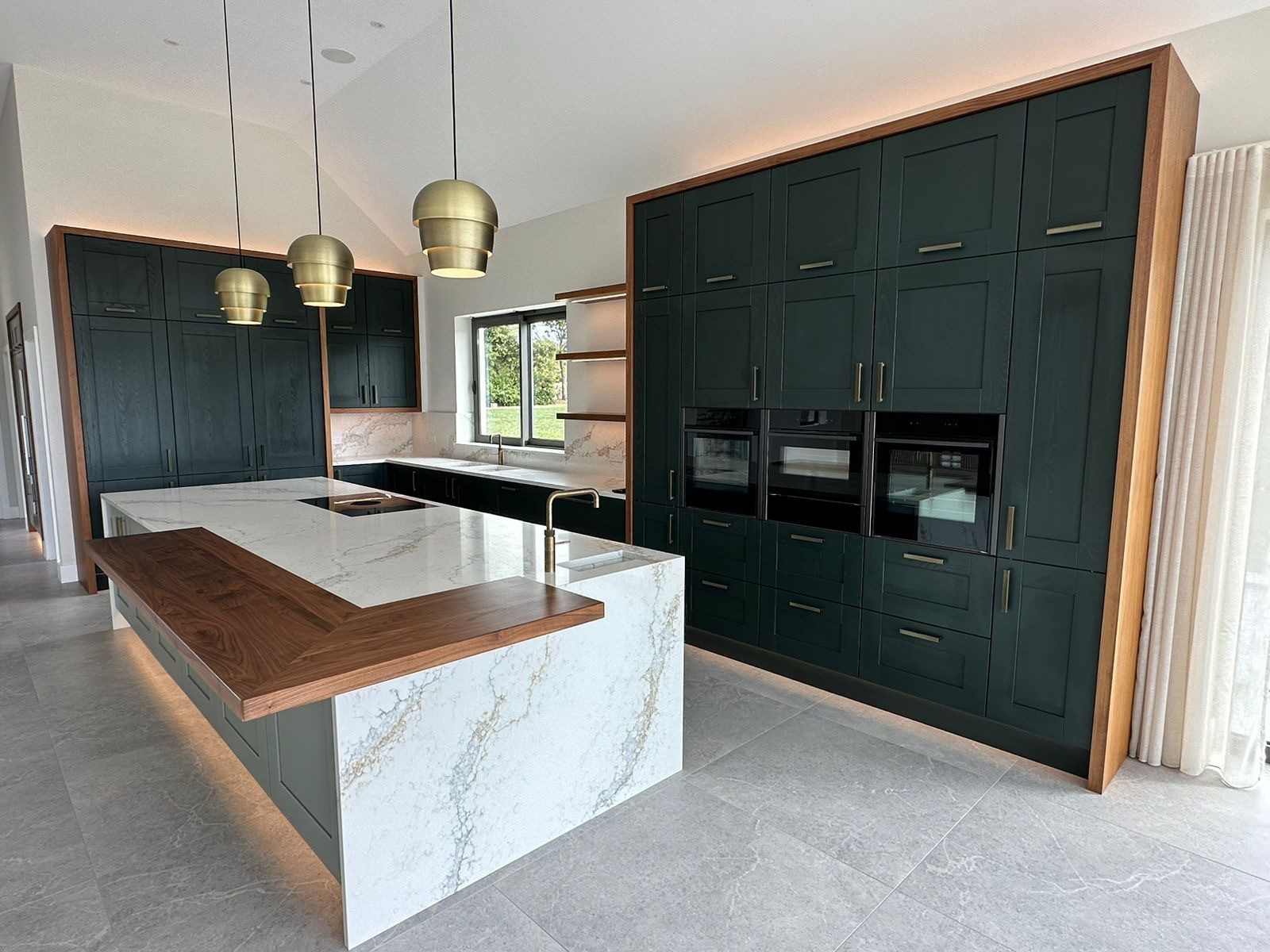 Modern kitchen with Calacatta-style quartz worktops, warm wood breakfast bar, and deep green cabinetry showcasing 2026 kitchen design trends.